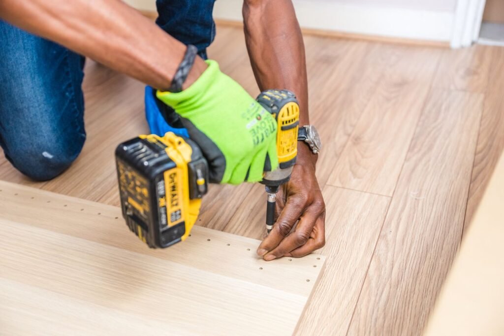 Close-up of handyman drilling wood indoors with green gloves and a nail gun.